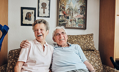 Ehepaar Mainert sitzt gemeinsam und lachend auf Couch