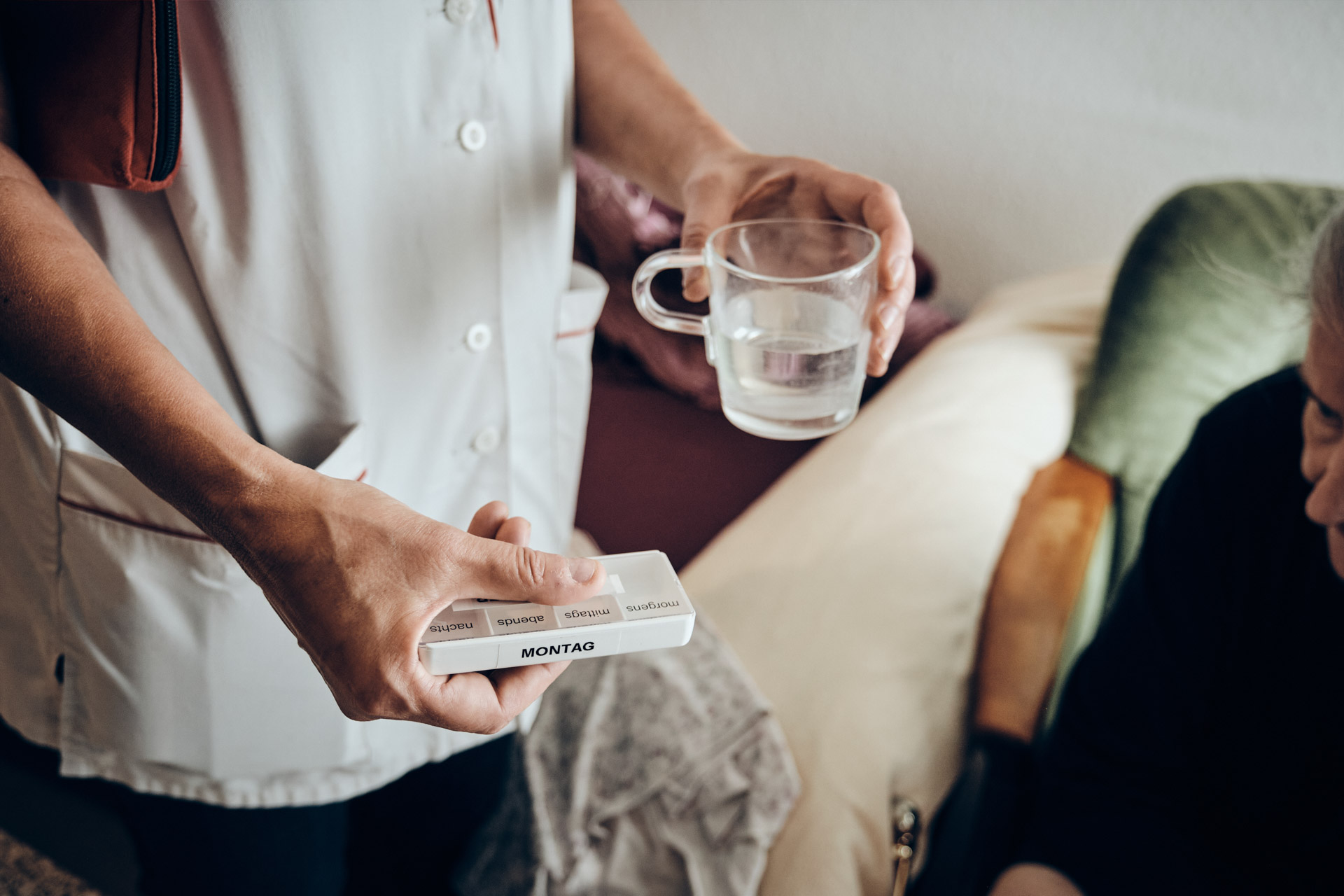 Pflegekraft mit Medikamenten in der einen Hand und einem Glas Wasser in der anderen Hand